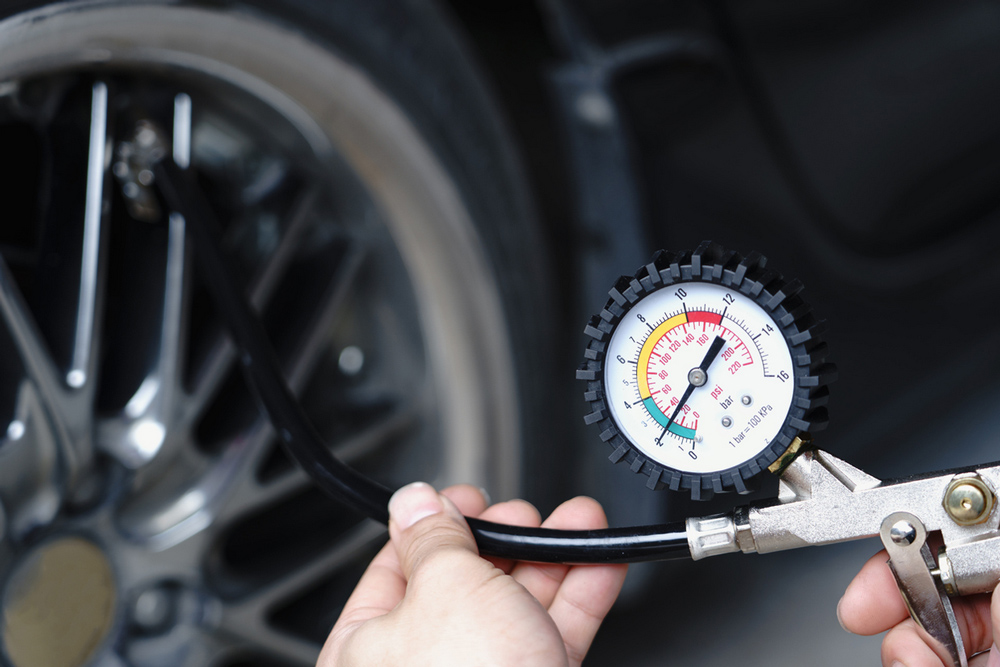 Driver holds a pressure gauge towards a tyre they are inflating.