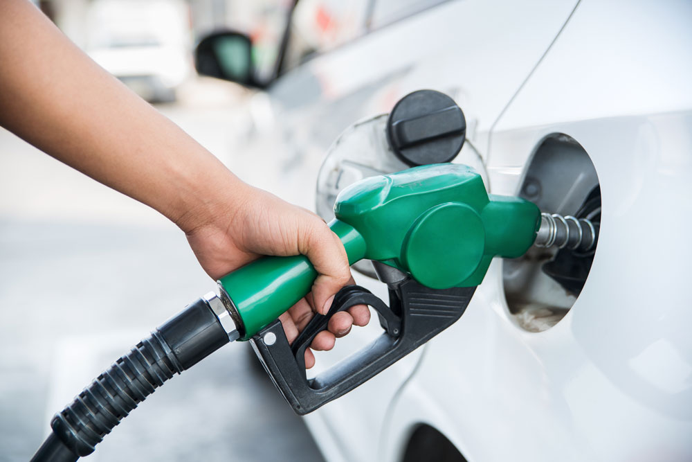 Person filling up their car with petrol using a green petrol pump.